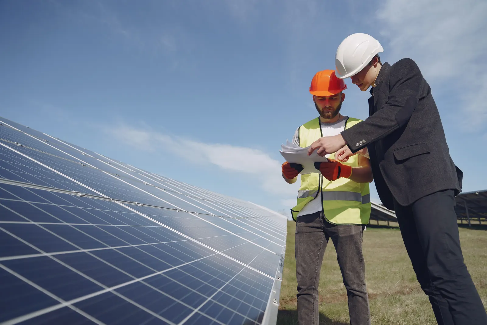 Técnicos con casco inspeccionando paneles solares y revisando documentos